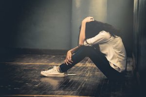 A woman sits hunched over on the floor as she contemplates her symptoms of depression