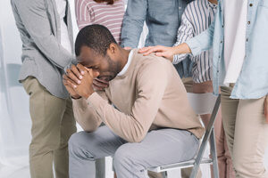 a therapy group comforts a man after talking about his trauma and substance abuse