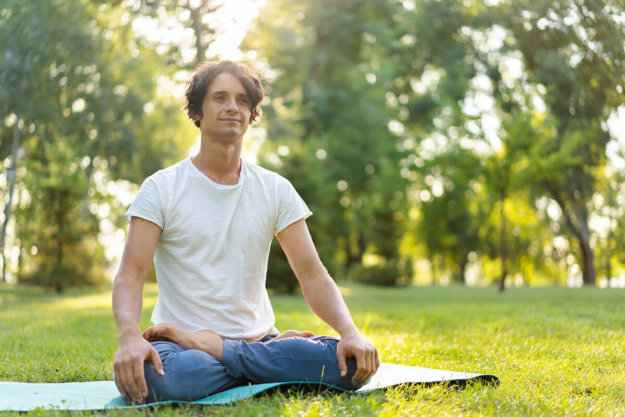 Young man meditating outdoors in the park man sitting on the grass practicing coping mechanisms
